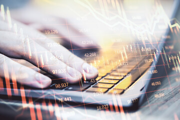 Hands typing on laptop keyboard with financial data charts overlay on bright background, symbolizing modern business and digital economy concept.