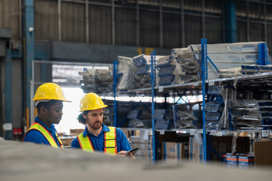 Two men warehouse worker wearing uniform and helmet safety standing using tablet checking stock products in warehouse factory store. Logistics, Distribution Center concept