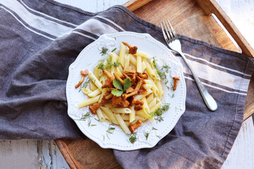  Penne pasta with fried in butter chanterelle mushrooms with garlic and finely chopped herbs on checkered napkin on a rustic background   © vaivirga