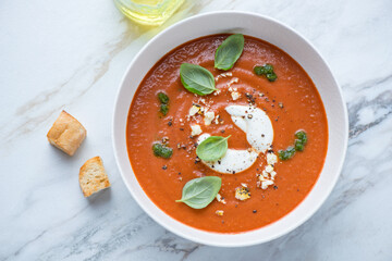 Bowl with roasted tomato and red bell pepper soup on a white stone background, horizontal shot, view from above