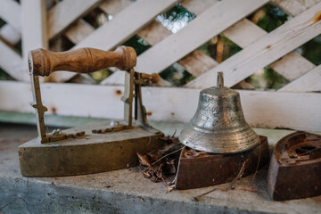 A vintage metal bell and antique flat iron sit on a weathered surface with dried leaves, evoking a nostalgic, rustic atmosphere..
