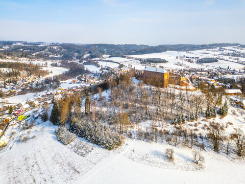 Pecka medieval castle stands proudly atop a hill, blanketed in snow. The surrounding landscape features frosted trees and quiet village below, creating a picturesque winter setting. - Powered by Adobe