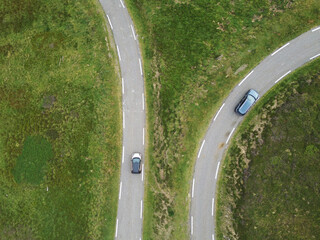two roads with two cars heading in two directions within green mountain landscape with fresh grass