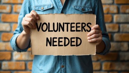 Man holding a cardboard sign with the words "Volunteers Needed"