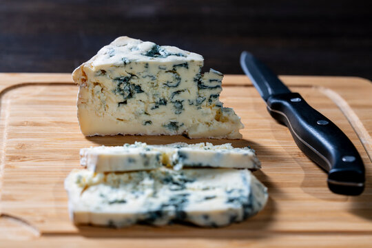 Pieces of blue cheese dorblu on a cutting wooden board and knife, closeup. Delicious blue cheese - Powered by Adobe