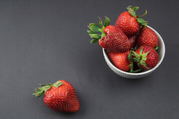 Strawberries lie in a gray bowl, one juicy berry lies on a black background. Farm food.