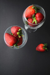 Juicy and large strawberries lie in glasses on a black background. Top view. Farm concept, healthy eating.