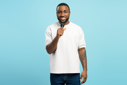 Smiling stylish African American performer singing with microphone on blue background