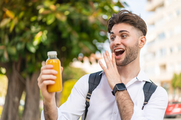 Fototapeta premium Young handsome man holding an orange juice at outdoors with surprise and shocked facial expression