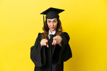 Middle aged university graduate isolated on yellow background points finger at you while smiling