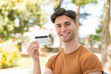 Fototapeta premium Young handsome man holding a credit card and thinking