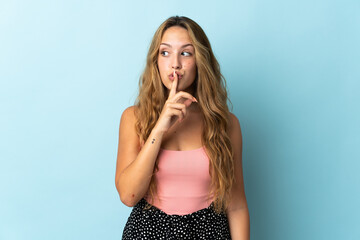 Young blonde woman isolated on blue background showing a sign of silence gesture putting finger in...