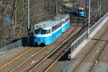 Fototapeta premium Tram travels through Gothenburg in spring with lush greenery surrounding the tracks and vehicles in motion