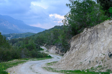 Winding dirt road through lush hills with dramatic clouds in the distance during early evening hours