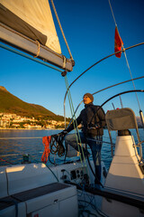 Young man captain standing at the helm and controls a sailboat during a journey by sea in winter time in Montenegro