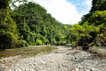 Wild river flowing through dense rainforest in the remote coastal region of Salat Rabia, Triton Bay, West Papua, Indonesia. A pristine tropical landscape of jungle and rocks.
