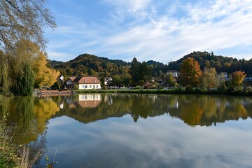 Obraz premium Autumnal village scene reflected in calm waters under a partly cloudy sky