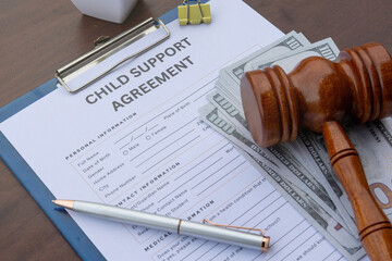 A detailed child support agreement paper on a desk with cash, a gavel, and a calculator,...
