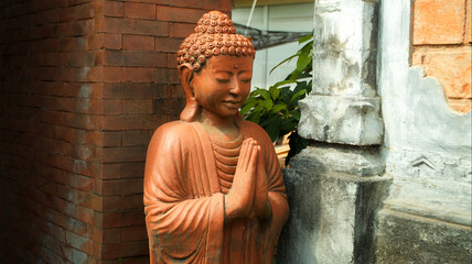 An old red clay statue of Buddha standing on the street on the bali