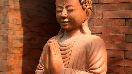 An old red clay statue of Buddha standing on the street on the bali
