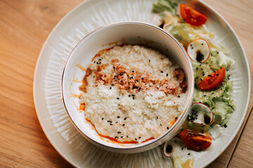 Savory oatmeal topped with fried bacon and parmesan served on a stylish plate with salad