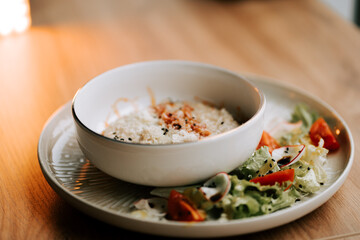 Savory oatmeal topped with fried bacon and parmesan served with a fresh salad
