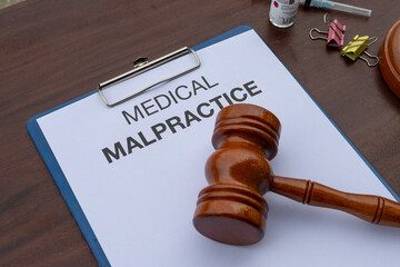 A clipboard holding a medical malpractice paper rests on a wooden desk, with a gavel nearby,...