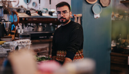 Obraz premium Male employee standing in a stylish cafe, surrounded by equipment, preparing food or beverages.