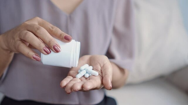 close-up of a woman's hand holding a medicine bottle and taking vitamin supplements like probiotics, zinc, or magnesium to help with her health, immunity, and overall wellness