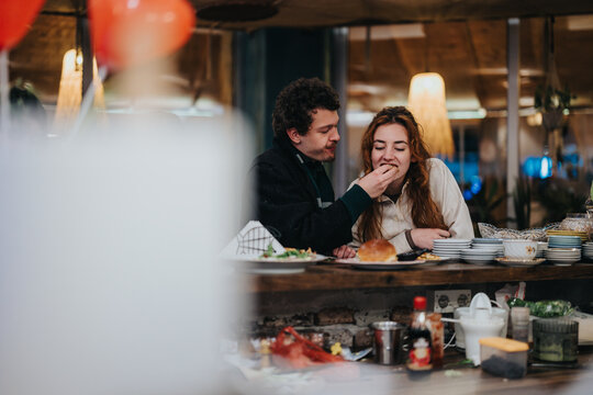A man and a woman sharing food in a cozy and warm lounge setting. The scene exudes feelings of togetherness, warmth, and casual dining with decorative backgrounds and plates.
