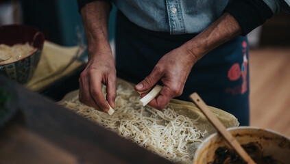 Close-up of hands layering pasta with grated cheese, showcasing a cooking process in a warm and inviting kitchen ambiance.