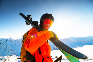 Portrait of young man with skis in snow at ski resort. Happy tourist relaxing on sunny day on top...