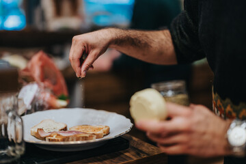 A person seasons an open-faced sandwich with precision and care. The scene captures the essence of homemade food preparation, emphasizing culinary expertise in a cozy kitchen environment.