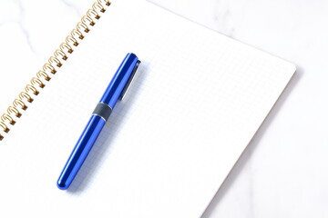 リング式のメモ帳とペンでデスクワークをしているイメージ
