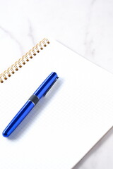 リング式のメモ帳とペンでデスクワークをしているイメージ
