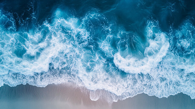 Aerial view of ocean waves crashing onto the shore with white foam and turquoise water surface.