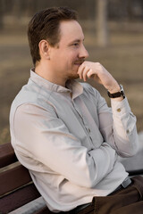 Portrait of an attractive Caucasian redhead young man sitting on a bench, smiling and thinking. A...