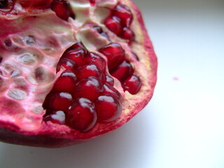 Close-up of a ripe pomegranate cut open to reveal juicy red seeds and textured interior against a...