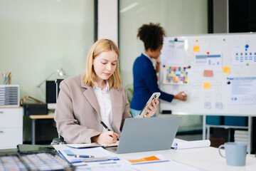 Confident business expert attractive smiling young woman typing laptop and holding digital tablet on desk