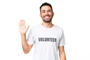 Young volunteer caucasian man over isolated chroma key background saluting with hand with happy expression