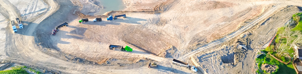 Panorama aerial view end dump, round bottom heavy-duty hauling trucks at construction site...