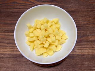 Fresh peeled potatoes that have been cut into small pieces, placed on a white ceramic bowl on a wooden table