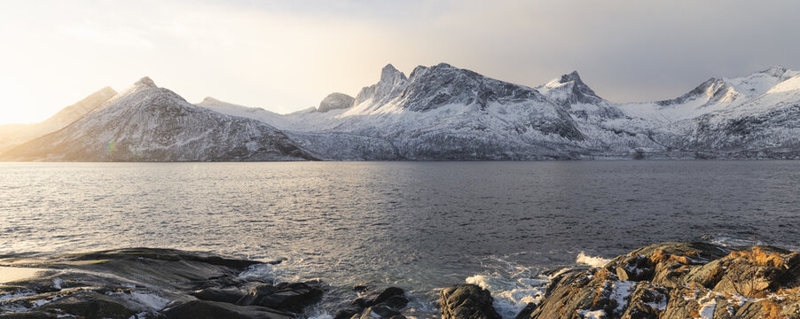 Sonnenlicht trifft auf die Bergkette westlich von Hus&oslash;y auf der Insel Senja in Norwegen und taucht die steilen Felsw&auml;nde in intensives Gelb, w&auml;hrend das tiefe Licht ihre Struktur deutlich hervorhebt