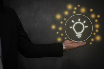 Businessman presenting a glowing light bulb icon in a dark setting, symbolizing innovation, creativity, and leadership. Ideal for business, technology, and visionary content themes.