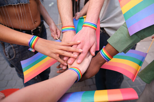 Diverse people joining hands at a LGBT pride parade, showing rainbow bracelets and flags, celebrating diversity and equality
