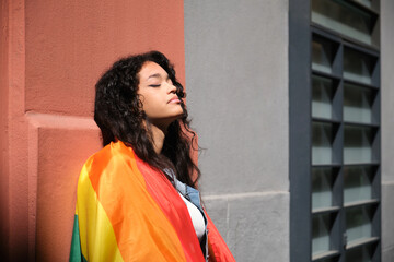 Young woman with closed eyes holding rainbow flag, celebrating LGBT pride and feeling sense of...
