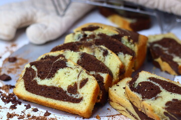 Slices of moist marble cake with chocolate and vanilla swirls, placed on a white surface.