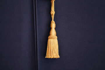 Golden tassel on elegant dark blue fabric. Close up decorative fringe. Classic interior detail....