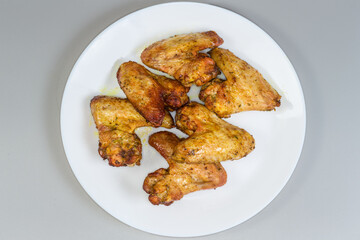 Baked chicken wings on dish on gray background, top view