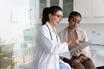 Positive mature Latin physician doctor showing checkup electronic result to young African patient...